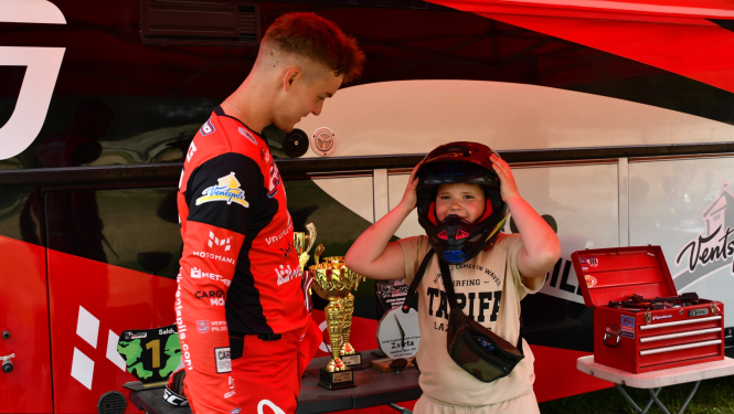 Motosportists palīdz bērnam uzmērīt ķiveri