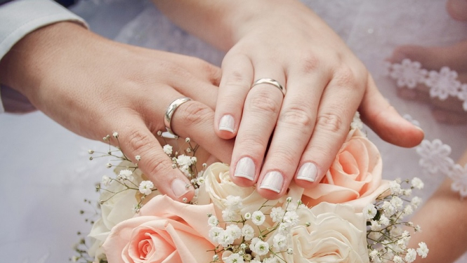 Rokas ar laulību gredzeniem uz pušķa