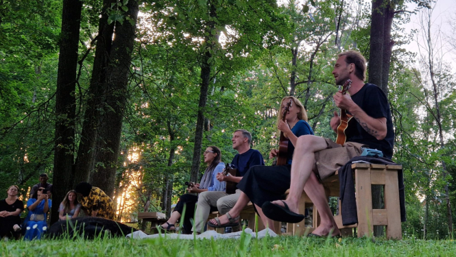 Cilvēki sēž uz soliņā, spēlē instrumentus un dzied