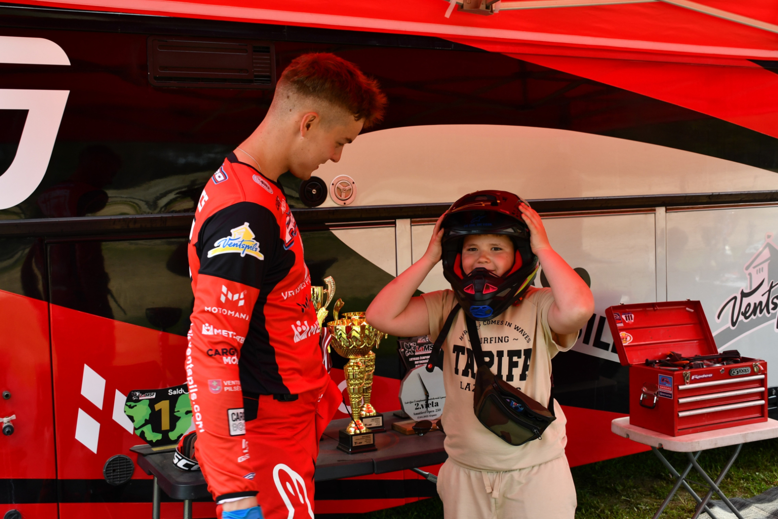 Motosportists palīdz bērnam uzmērīt ķiveri