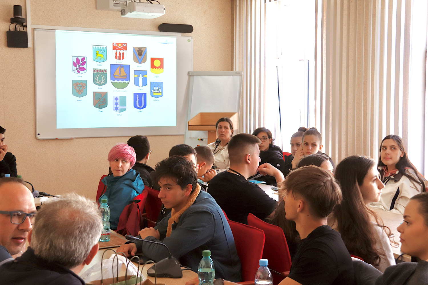 Projekta dalībnieki skatās prezentāciju