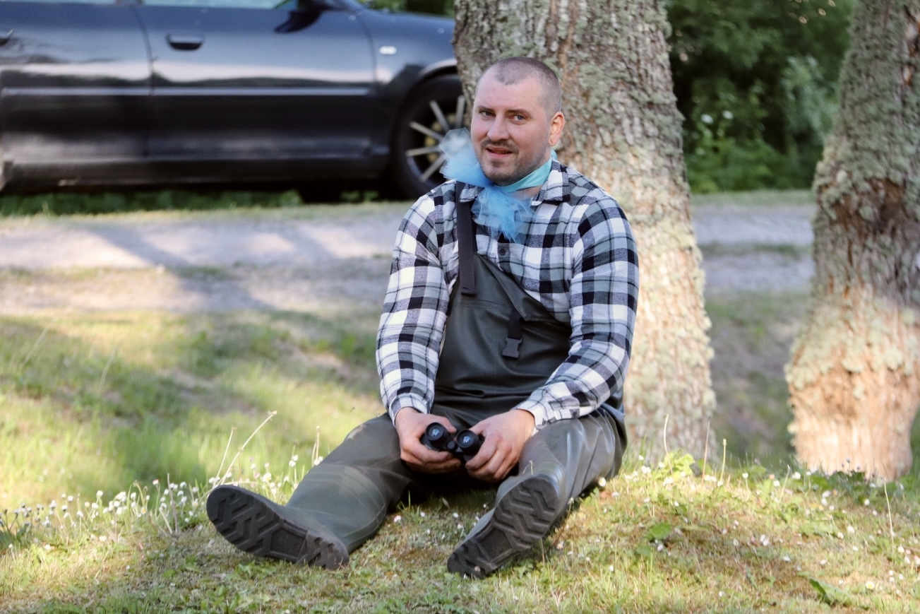 Vīrietis kostīmā sēž zem koka